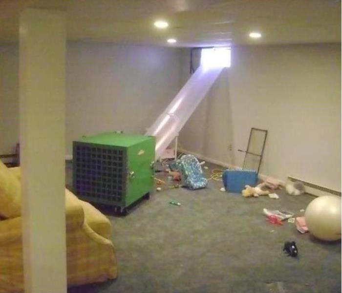 basement with grey carpet and green dehumidifier setup with a plastic vent going to a window