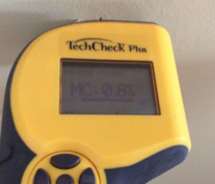 yellow moisture meter stuck into a white wall