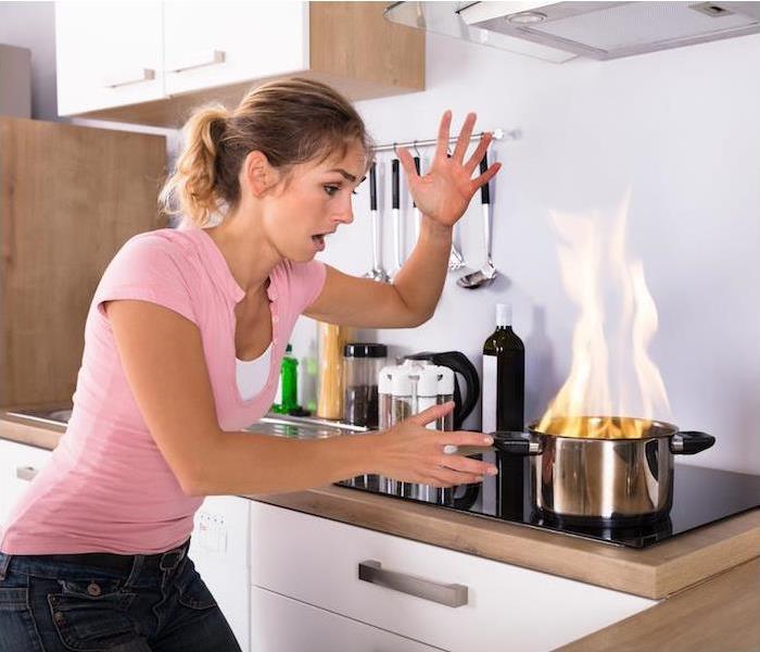 Blonde woman in a pink shirt reacting frantically to a pot that has caught on fire on her glass cooktop